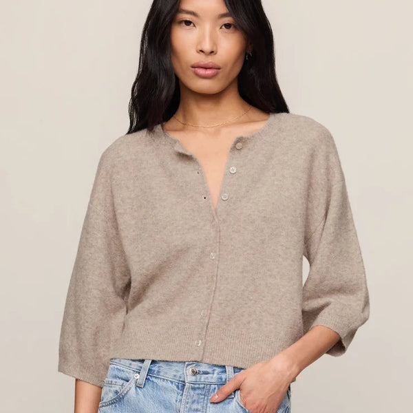 Woman wearing a beige cardigan and light blue jeans against a plain background