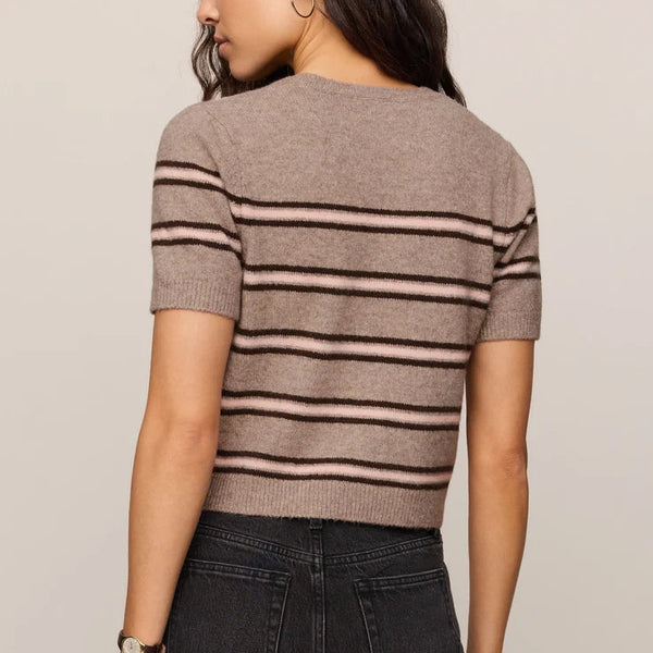 A woman shown from the back wearing a short-sleeve knit top with horizontal taupe and black stripes, paired with dark gray jeans, against a plain light beige studio background.