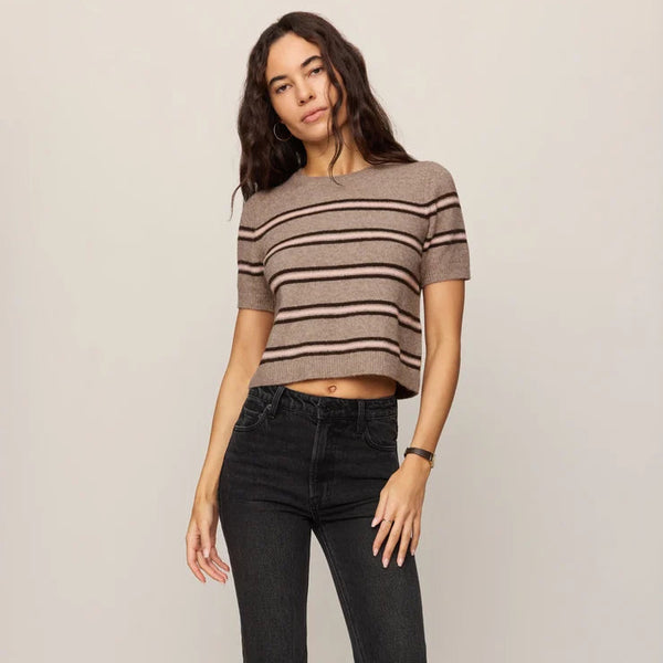 Woman wearing a striped sweater and black jeans against a plain background