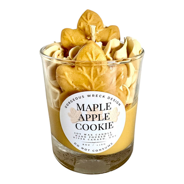 Candle in a glass jar labeled 'Maple Apple Cookie' with leaf-shaped cookies on top.