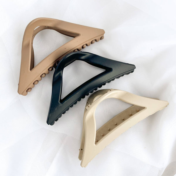 Three triangle-shaped hair clips in beige, black, and gold on a white background