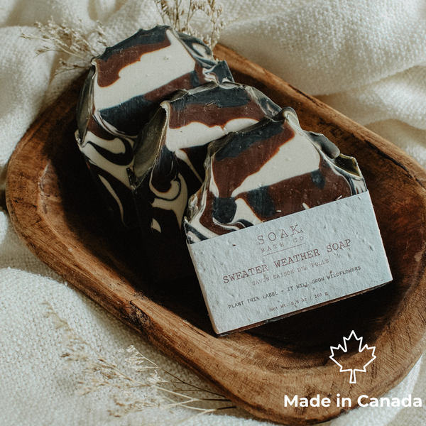 Three bars of handmade soap with a black, white, and brown marble pattern are arranged on a rustic wooden tray. A paper label on the front bar reads 'SOAK Farm Co.
