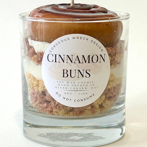 Candle in a glass jar labeled 'Cinnamon Buns' with a decorative top on a white background.
