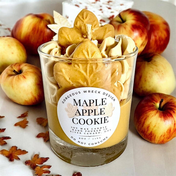 Maple apple cookie candle in a glass jar with apples and autumn leaves around it.