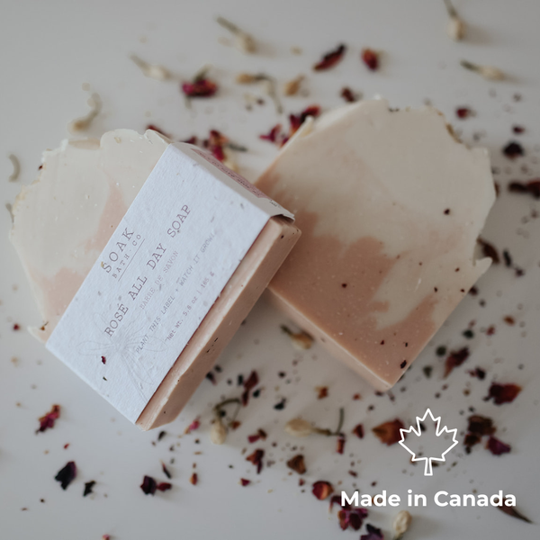 Bar of soap with a box labeled 'Rose All Day Soap' on a textured surface with dried flowers, and 'Made in Canada' label.