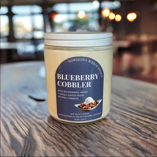 Jar of 'Blueberry Cobbler' candle on a wooden table with a blurred background