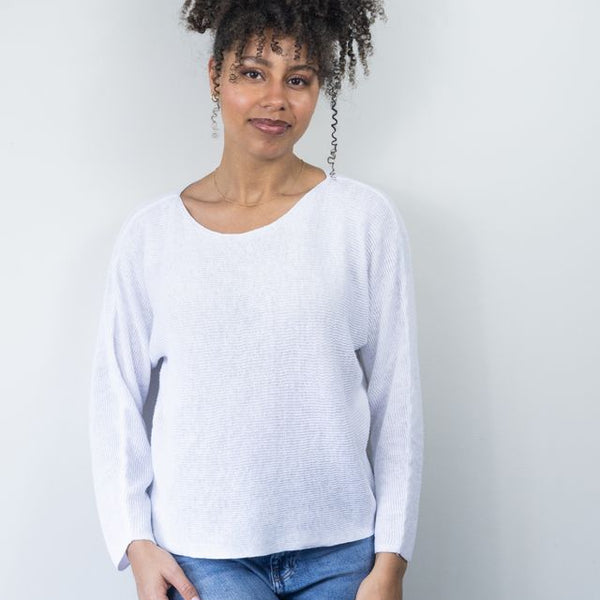 Woman wearing a white sweater and blue jeans against a plain background