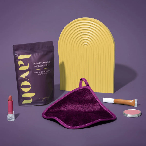 Makeup removal products including a reusable makeup remover cloth, lipstick, and other items on a purple background.