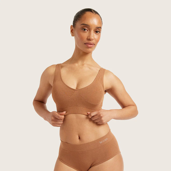 Woman wearing a brown sports bra and high-waisted underwear on a light background