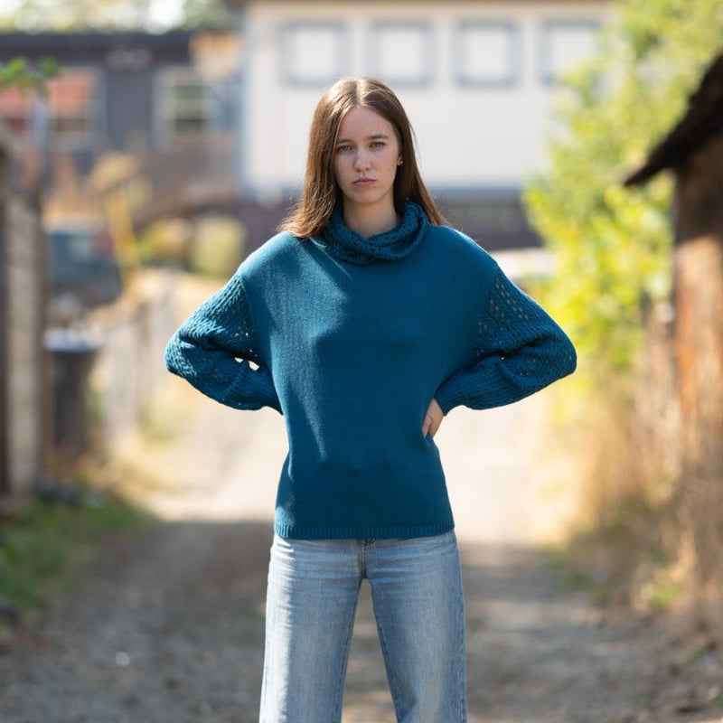 Woman wearing a blue sweater and jeans standing on a dirt path with blurred background