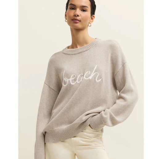 Woman wearing a beige sweater with 'beach' text on a plain background