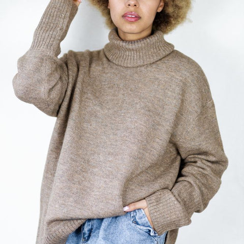 Woman wearing a beige sweater and light blue jeans against a white background