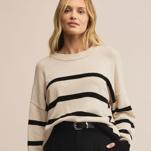 Woman wearing a cream sweater with black stripes and black pants on a beige background