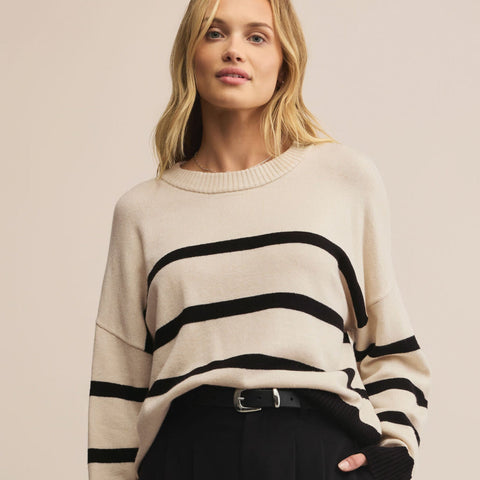 Woman wearing a cream sweater with black stripes and black pants on a beige background