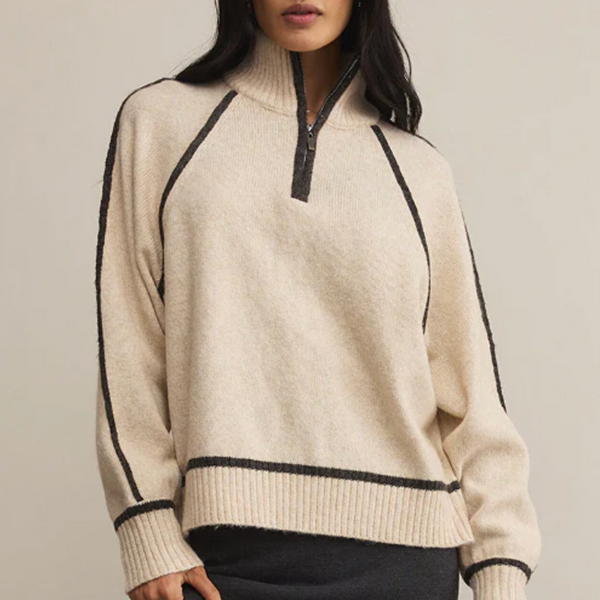 Woman wearing a beige sweater with black accents on a plain background