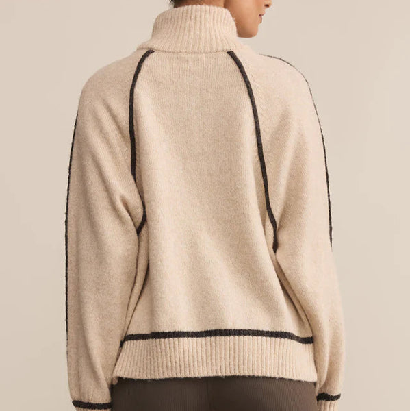 Woman wearing a beige sweater with black accents on a beige background